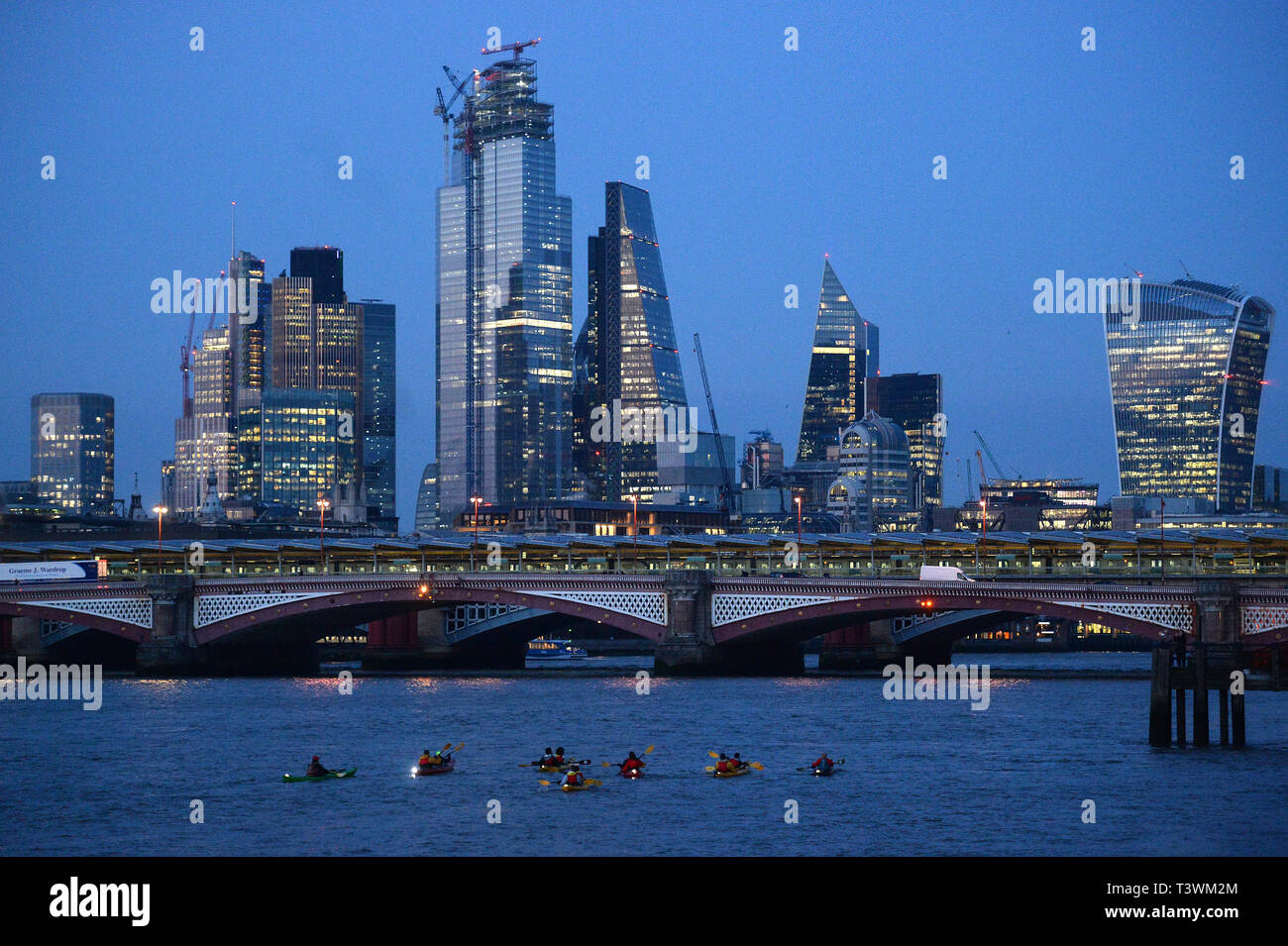 People canoe and kayak down the River Thames in front of the City of