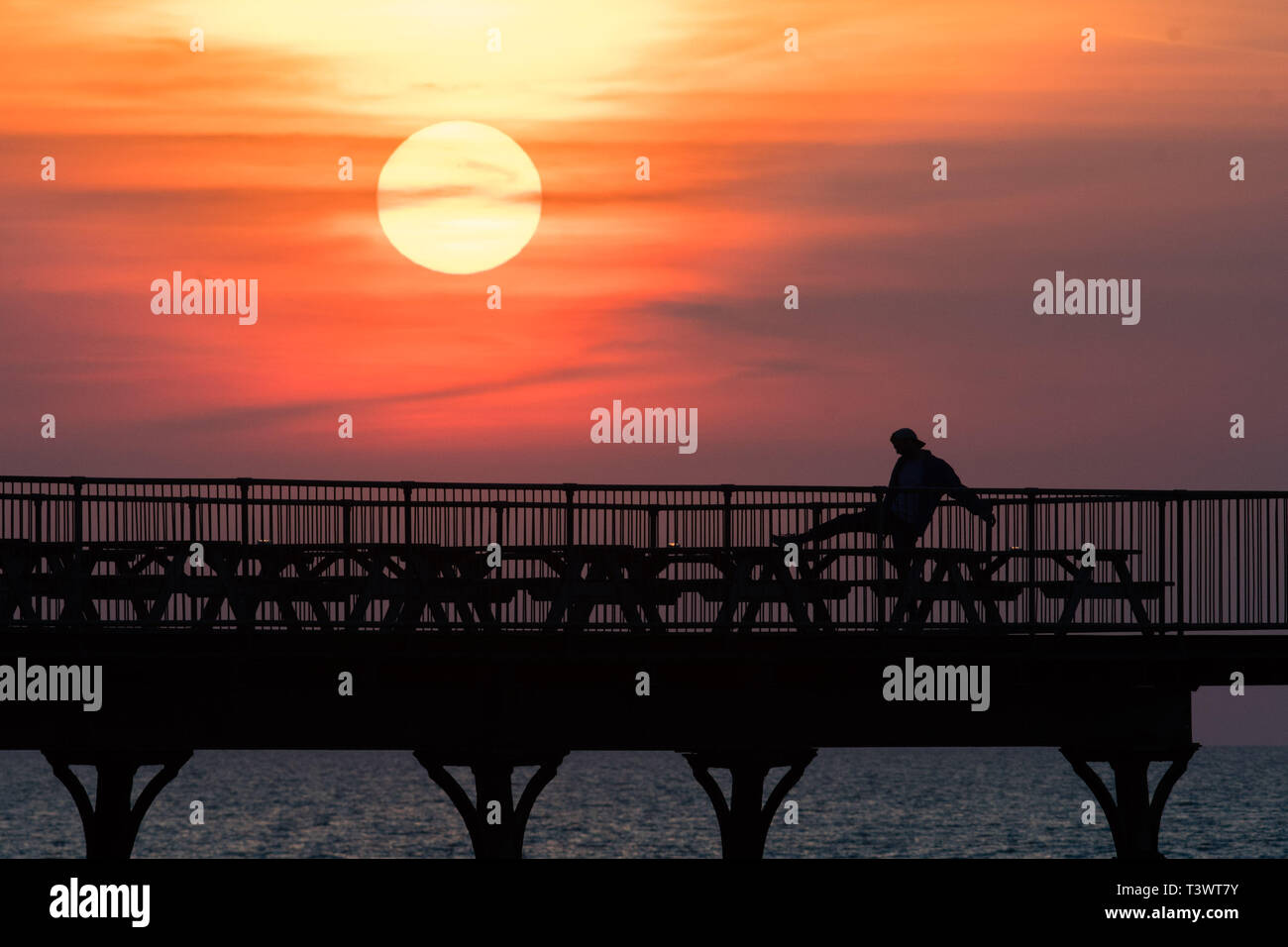 Aberystwyth Wales UK. 11 April 2019. UK Weather: The sun sets as a spectacular golden  globe behind  people silhouetted as they stand at the end of the pier in Aberystwyth on the Cardigan Bay coast of west Wales. Credit: Keith Morris/Alamy Live News Stock Photo