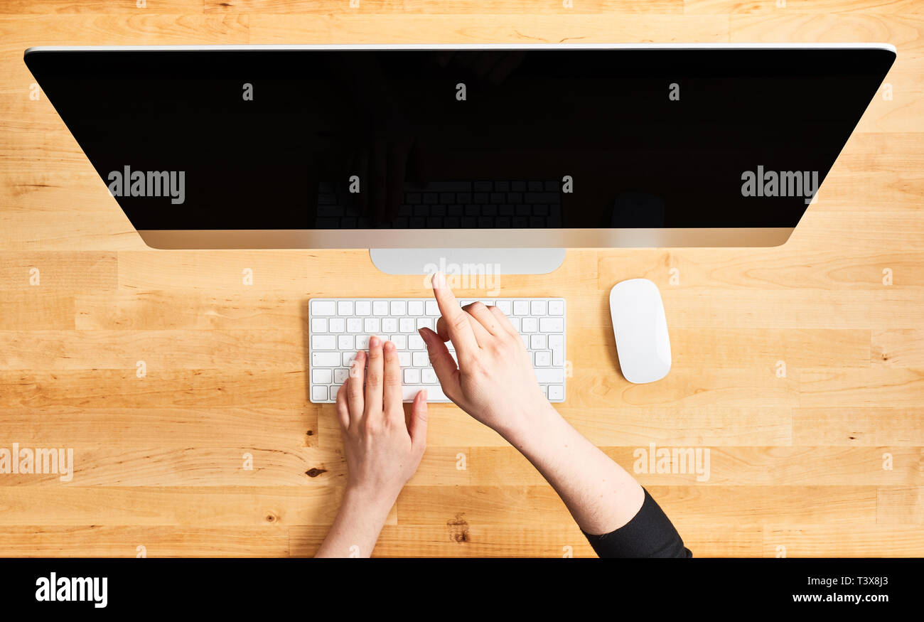 Female hands pointing at desktop computer. Top view of wooden office desk with large desktop computer, female hands on the keyboard and mouse. All in  Stock Photo