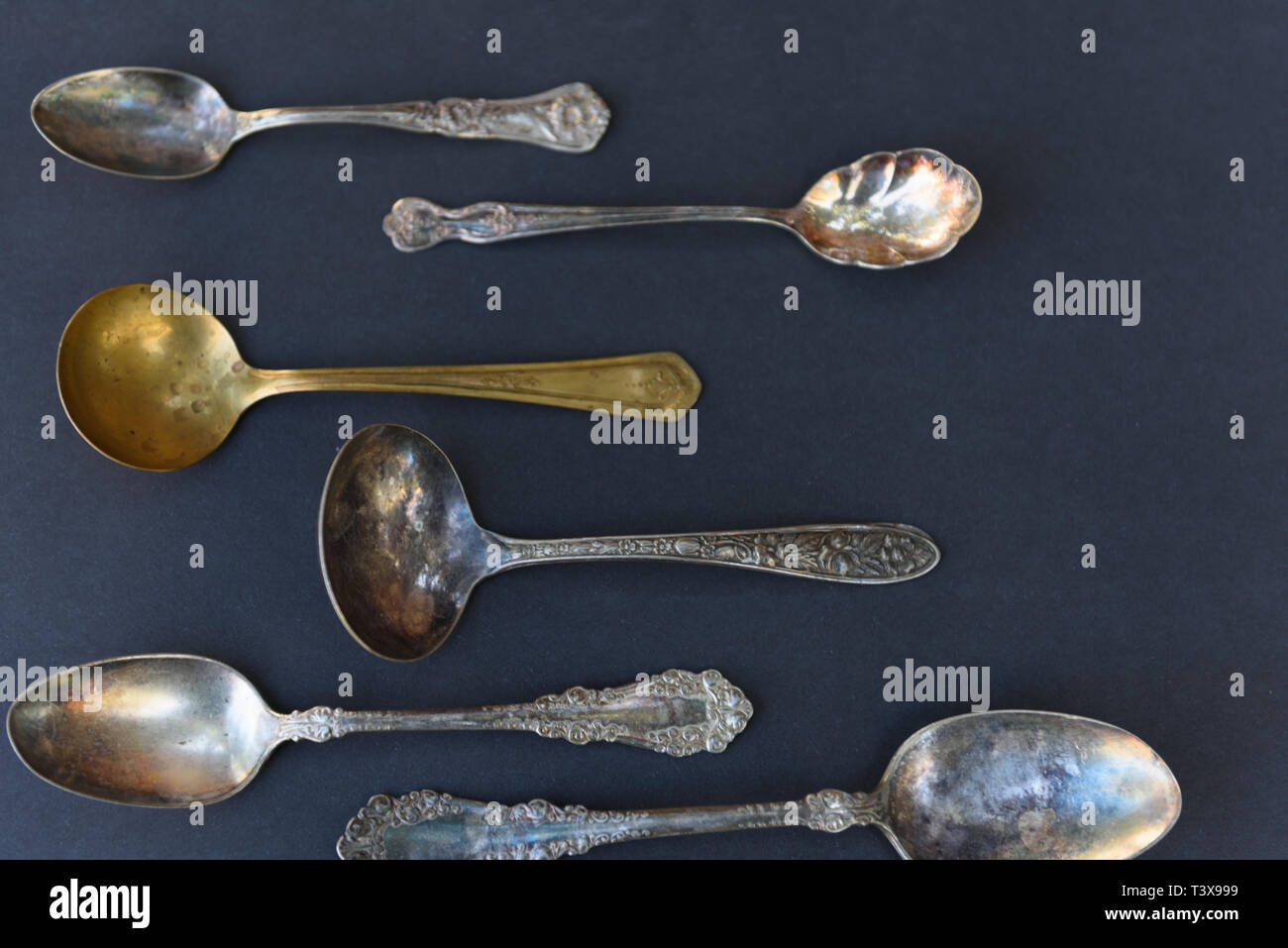 Weathered silverware of multiple sizes and patterns are arranged against a black background. Stock Photo