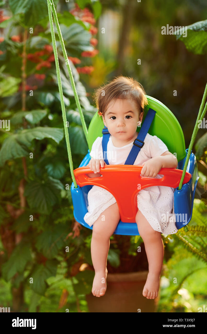 Baby girl on swings on blurred green garden background Stock Photo