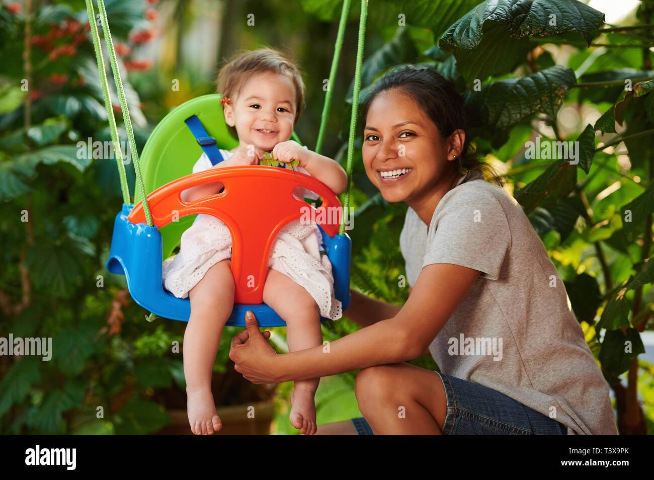 Smiling girl nurse play with baby on swings Stock Photo