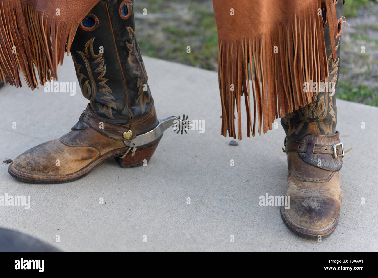 Old worn cowboy boots with spurs on an old cowboy wearing leather chaps. Stock Photo