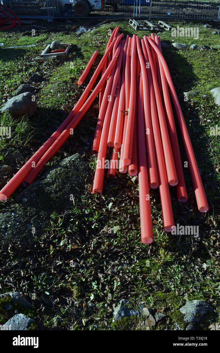 Stack red plastic electricity cable protection pipes near street on lawn Stock Photo