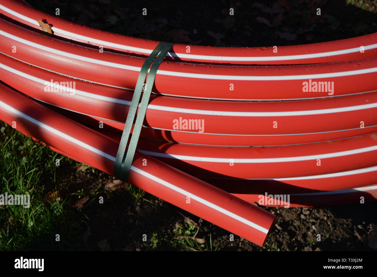 Roll red newe plastic electricity cable protection pipes on street Stock Photo