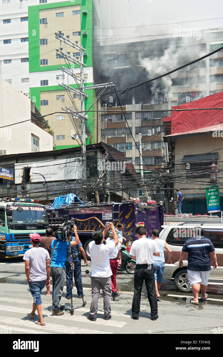 Manila, Philippines: Deadly fire in an apartment building in Binondo with group of men and camera man watching near firetrucks Stock Photo