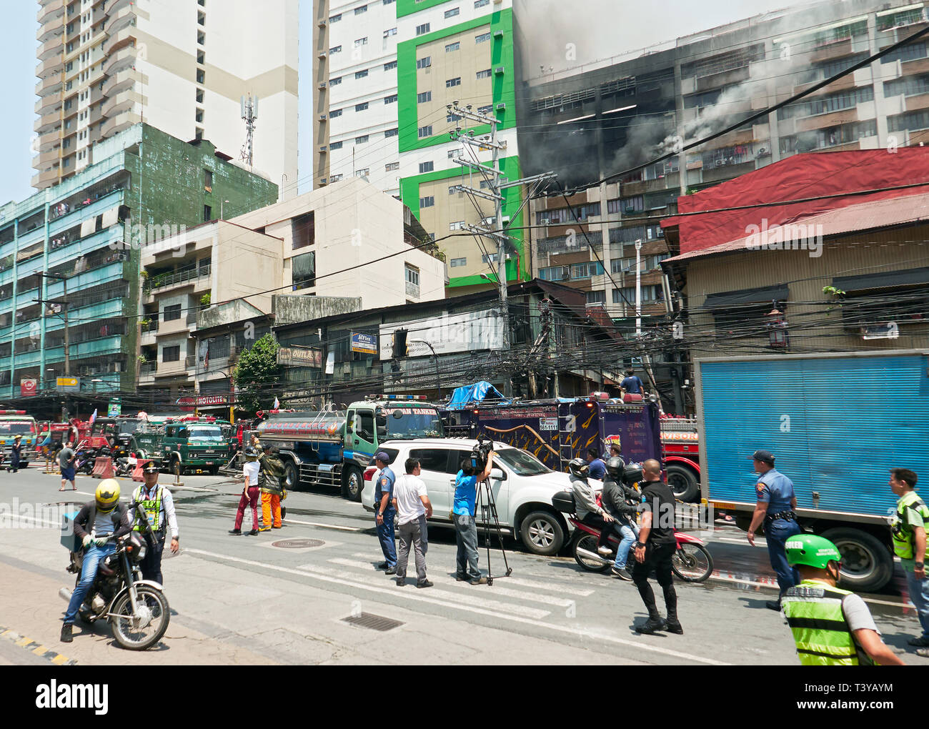 Manila, Philippines: Deadly fire in an apartment building in Binondo with group of men and camera man watching near firetrucks Stock Photo