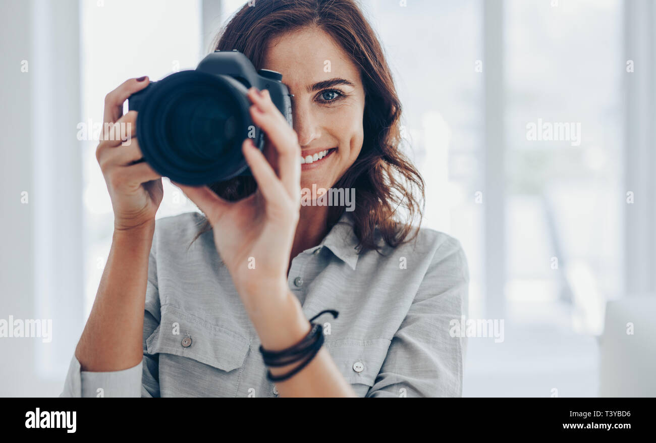 Woman with dslr camera photographing indoors taking few pictures. Happy female photographer taking pictures with professional camera. Stock Photo