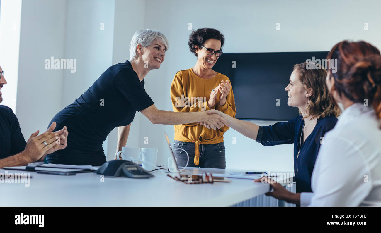 Businesswomen shaking hands and smiling during a business meeting with team clapping hands. Team congratulating and appreciating the performance of a  Stock Photo