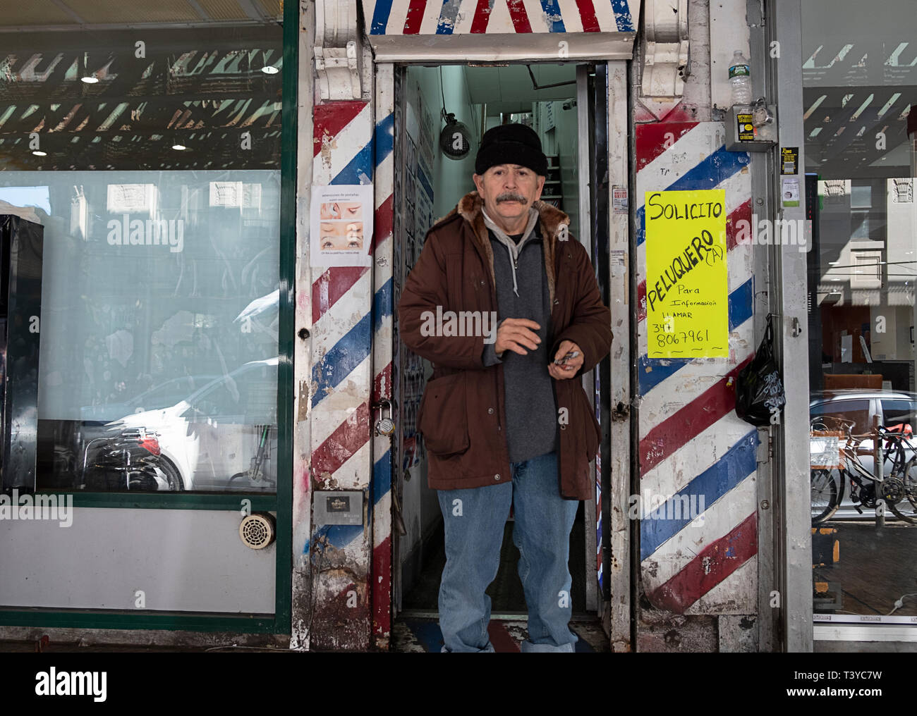 A man standing in front of a barber shop handing out business promotional cards. On Roosevelt Ave. in Jackson Heights, Queens, New York Stock Photo