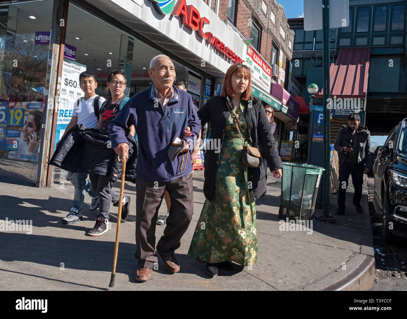 A young Asian woman walks arm in arm with an older man, presumably her grandfather. On 74th St. in Jackson Heights, Queens, New York City. Stock Photo
