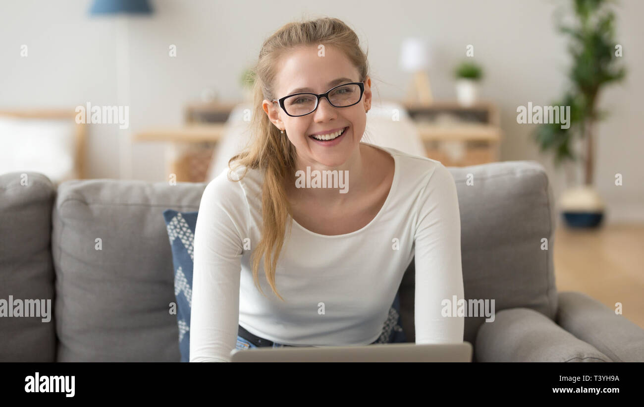 Head shot portrait of smiling woman in glasses, sitting on sofa at home ...