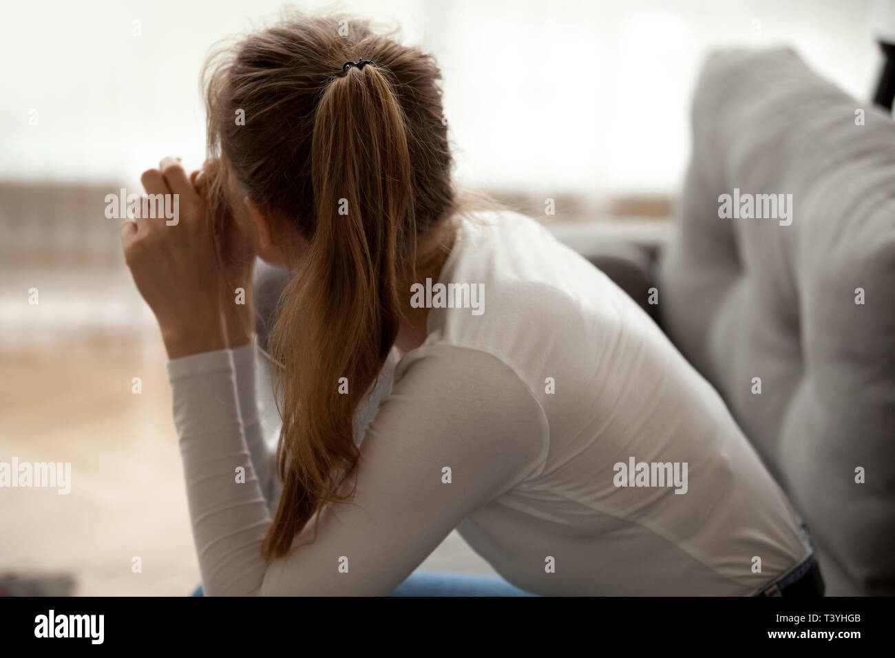 Rear view pensive thoughtful woman sitting on sofa, lost in thoughts Stock Photo