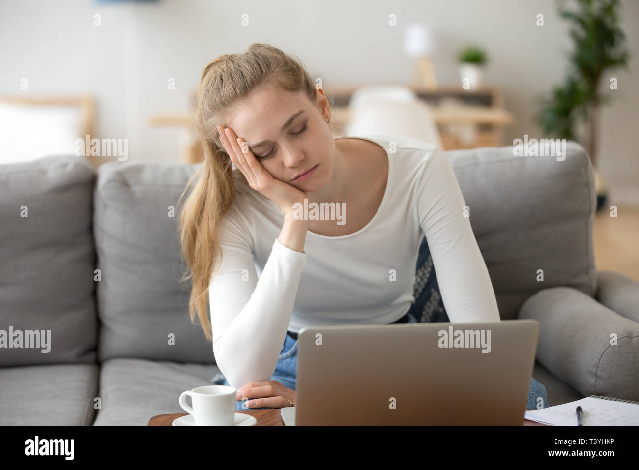 Bored sleepy woman holding head on hand, sitting with laptop Stock Photo