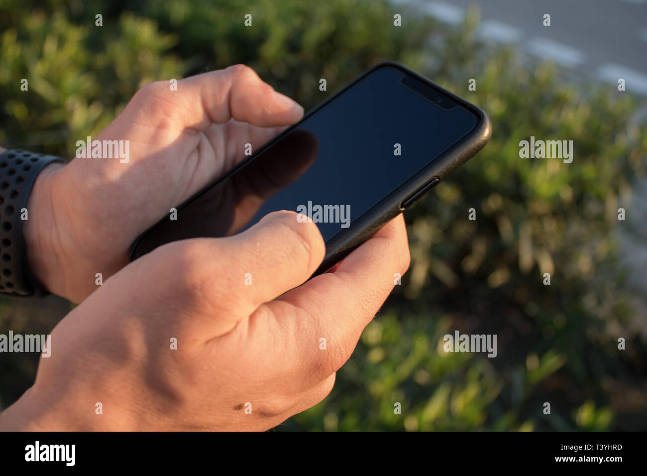 Hands of a young person using his smartphone on the outside. It's the sunset. Person sending a text message and checking social networks. Stock Photo