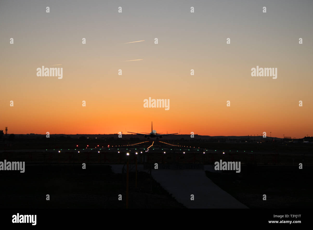 4K. Passenger airplane is landing on the airport runway during sunset. The sky is orange. Silhouette of an airplane that is landing. Stock Photo