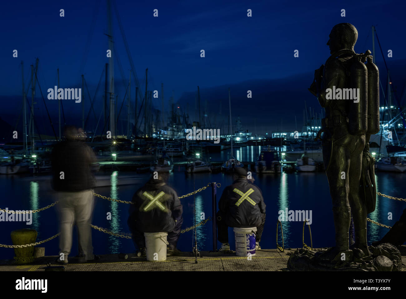 Fishermen at the Simons Town marina in South Africa's Western Cape province in the shadow of the Standby Diver bronze sculpture memorial Stock Photo