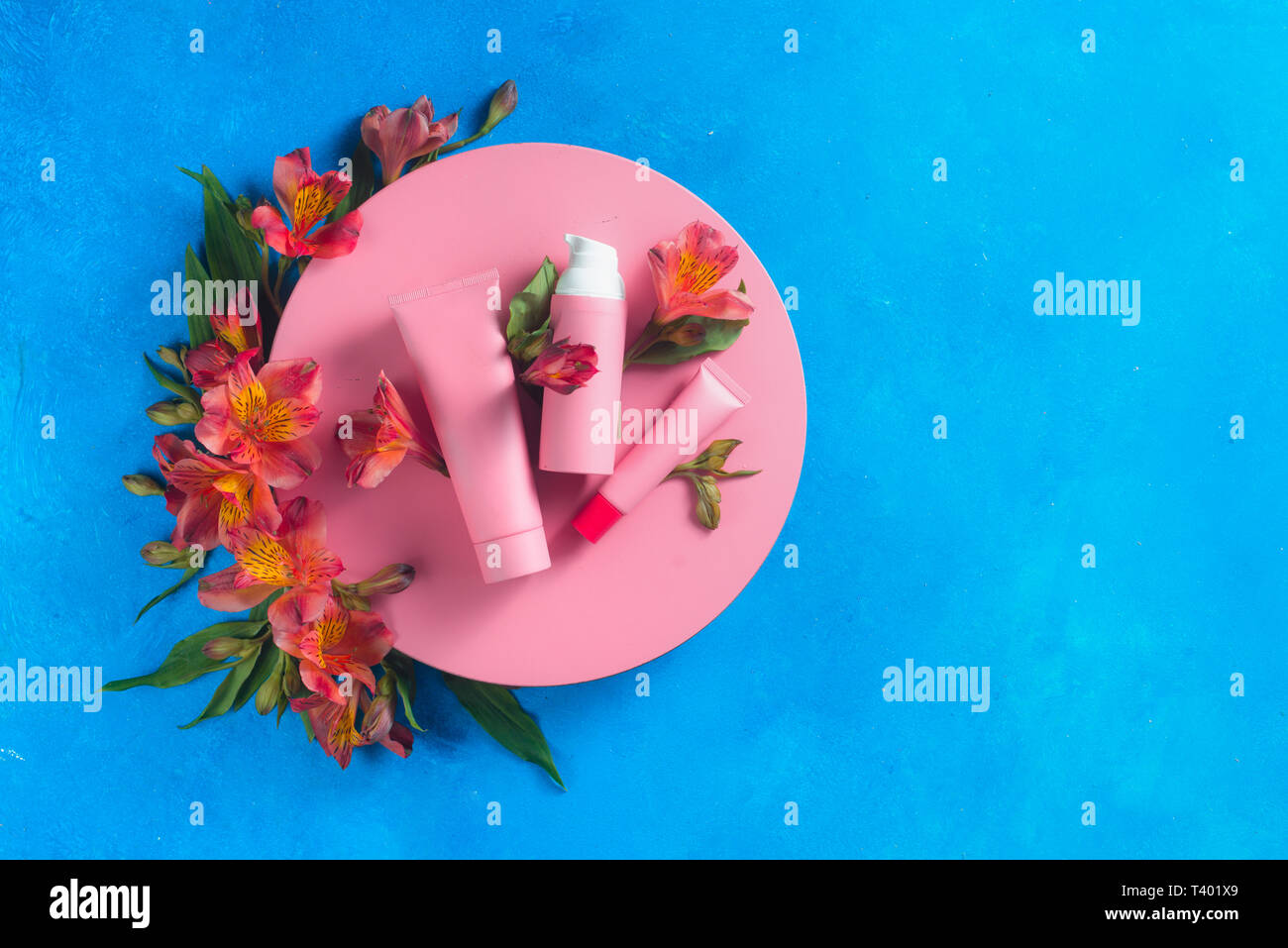 Sunscreen and skin care cosmetics in the pink palette in on a blue background with spring alstroemeria flowers. Pink circle flat lay Stock Photo
