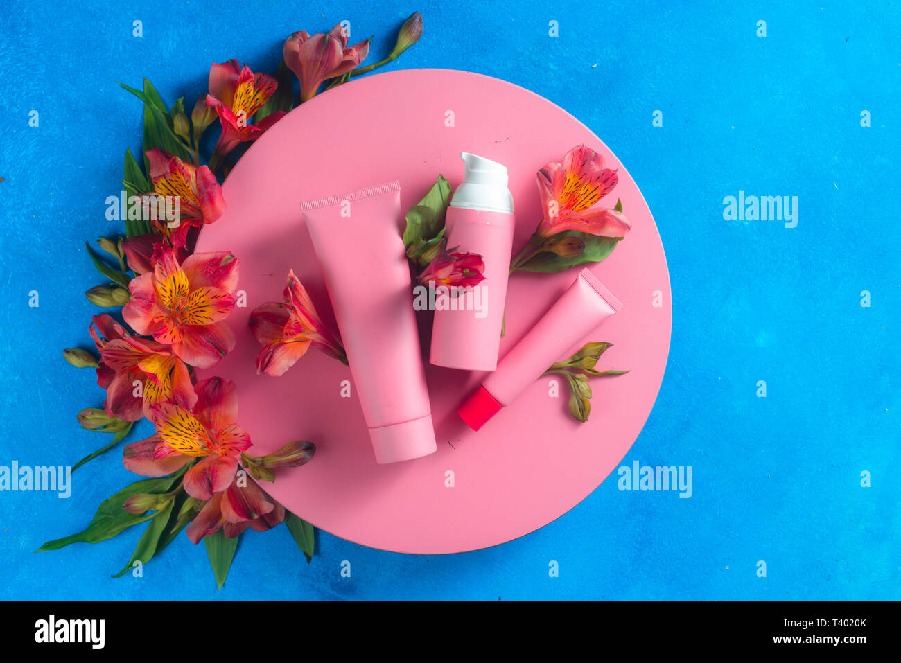 Sunscreen and skin care cosmetics in the pink palette in on a blue background with spring alstroemeria flowers. Pink circle flat lay Stock Photo