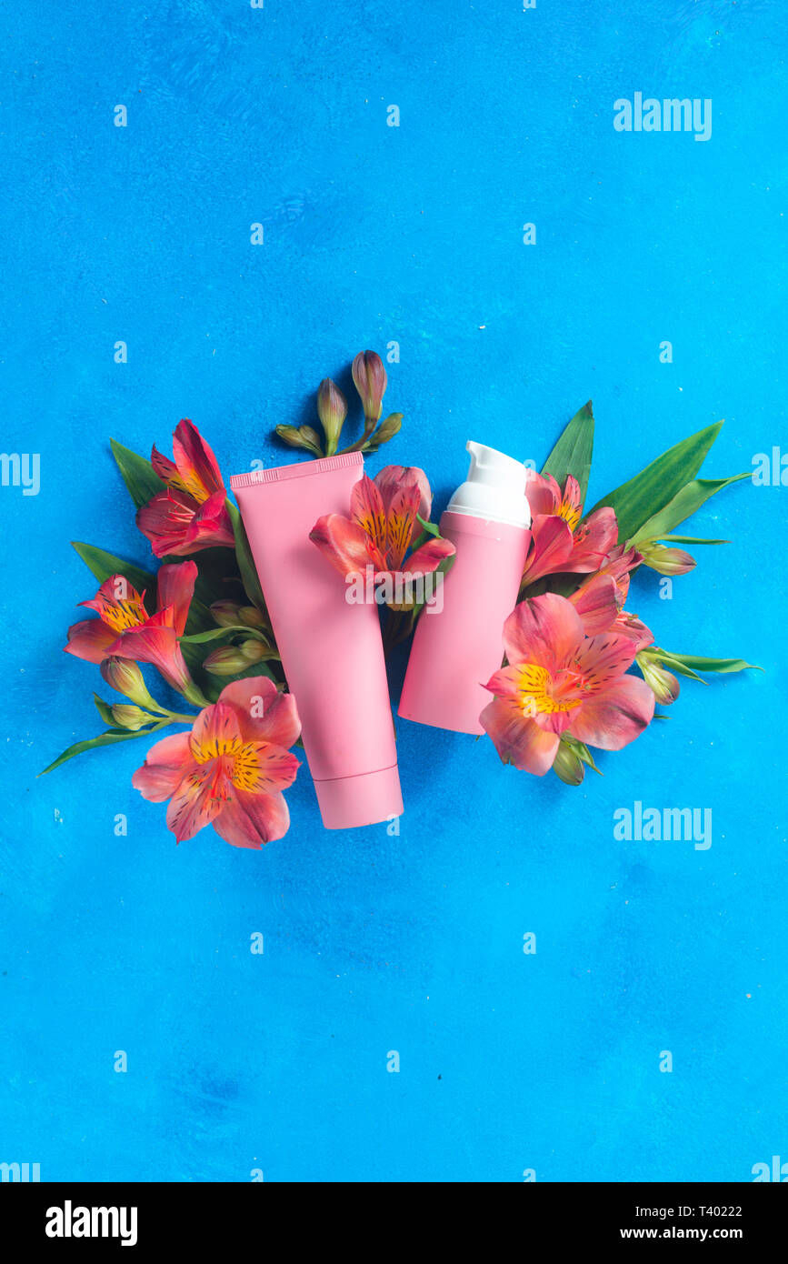 Skin care cosmetics in pink palette in on a blue background with spring flowers. Natural cosmetics conceptual flat lay with copy space Stock Photo