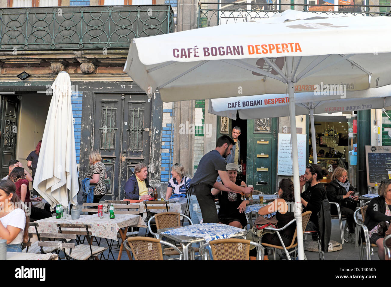 Waiter serving people customers sitting eating alfresco outside at tables at the Cafe Bogani Desperta in Porto, Portugal Europe EU  KATHY DEWITT Stock Photo