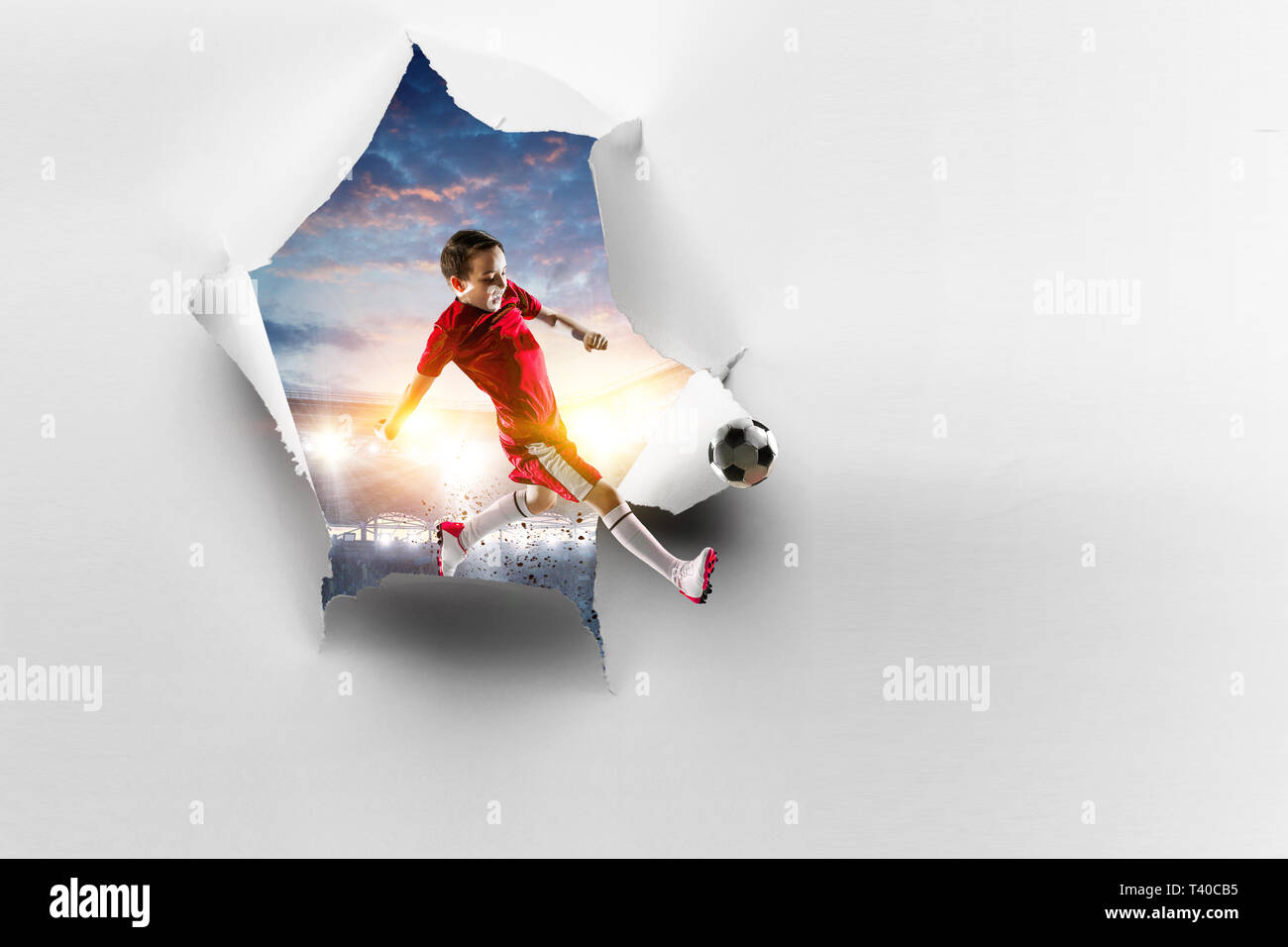 Paper torn hole effect and a kid playing soccer. Mixed media Stock