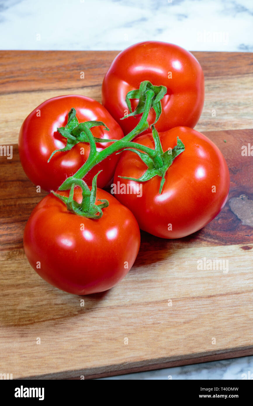 Tomatoes on a green vine laying on a wooden cuttung board Stock Photo ...
