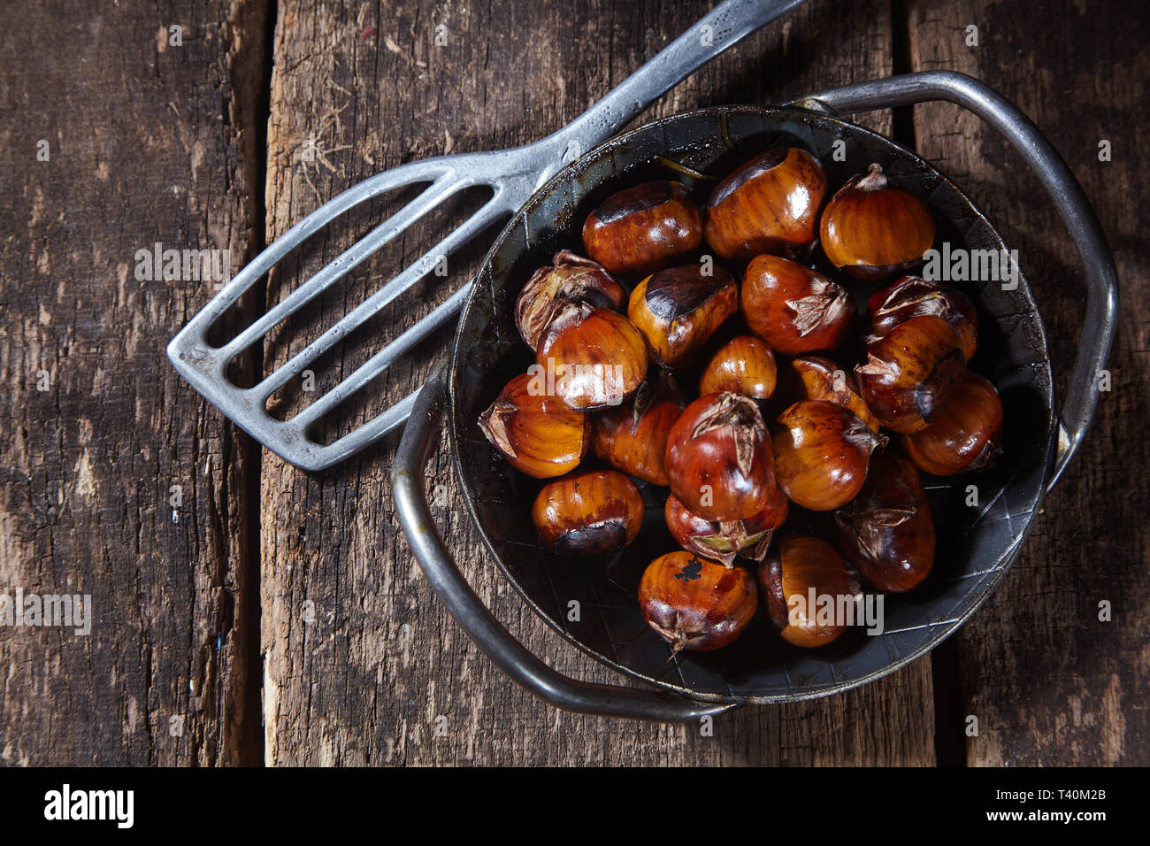 Old cast iron dish full of roasted chestnuts with a spatula alongside