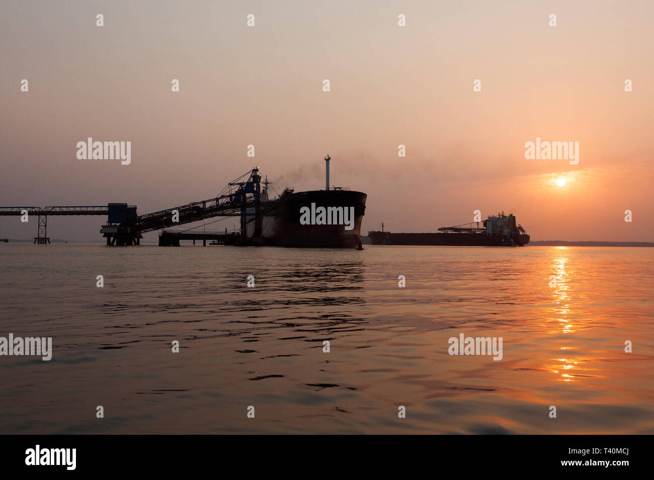 Port operations for managing and transporting iron ore at dawn and sunrise with 2 TSV ships - one at loading jetty, one waiting to dock. Sierra Leone Stock Photo