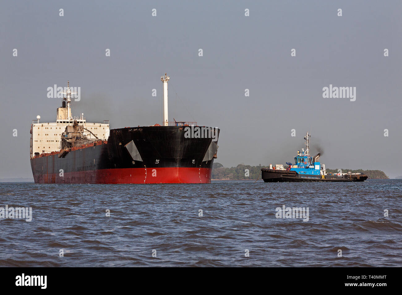Port operations for managing and transporting iron ore. Transhipping boat and tug prepare to set sail to unload into OGV - Ocean Going Vessel at sea Stock Photo