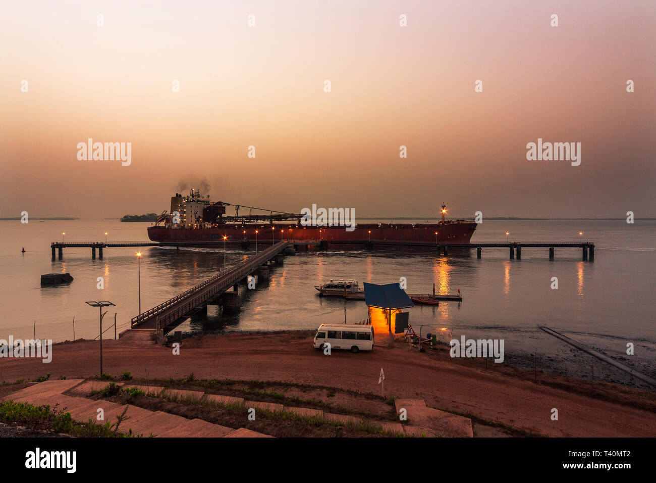 Port operations for managing and transporting iron ore at dawn. TSV ship unberthing from layby jetty to move and load at loading jetty. Sierra Leone Stock Photo