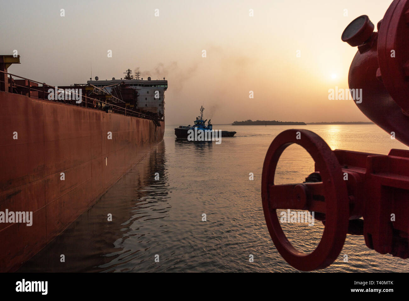 Sunrise during port operations managing and transporting iron ore. Ship to ship moving and berthing operation from tug to leading tug prior to sailing Stock Photo