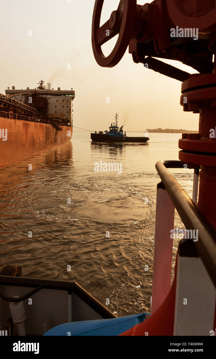Sunrise during port operations managing and transporting iron ore. Ship to ship moving and berthing operation from tug to leading tug prior to sailing Stock Photo