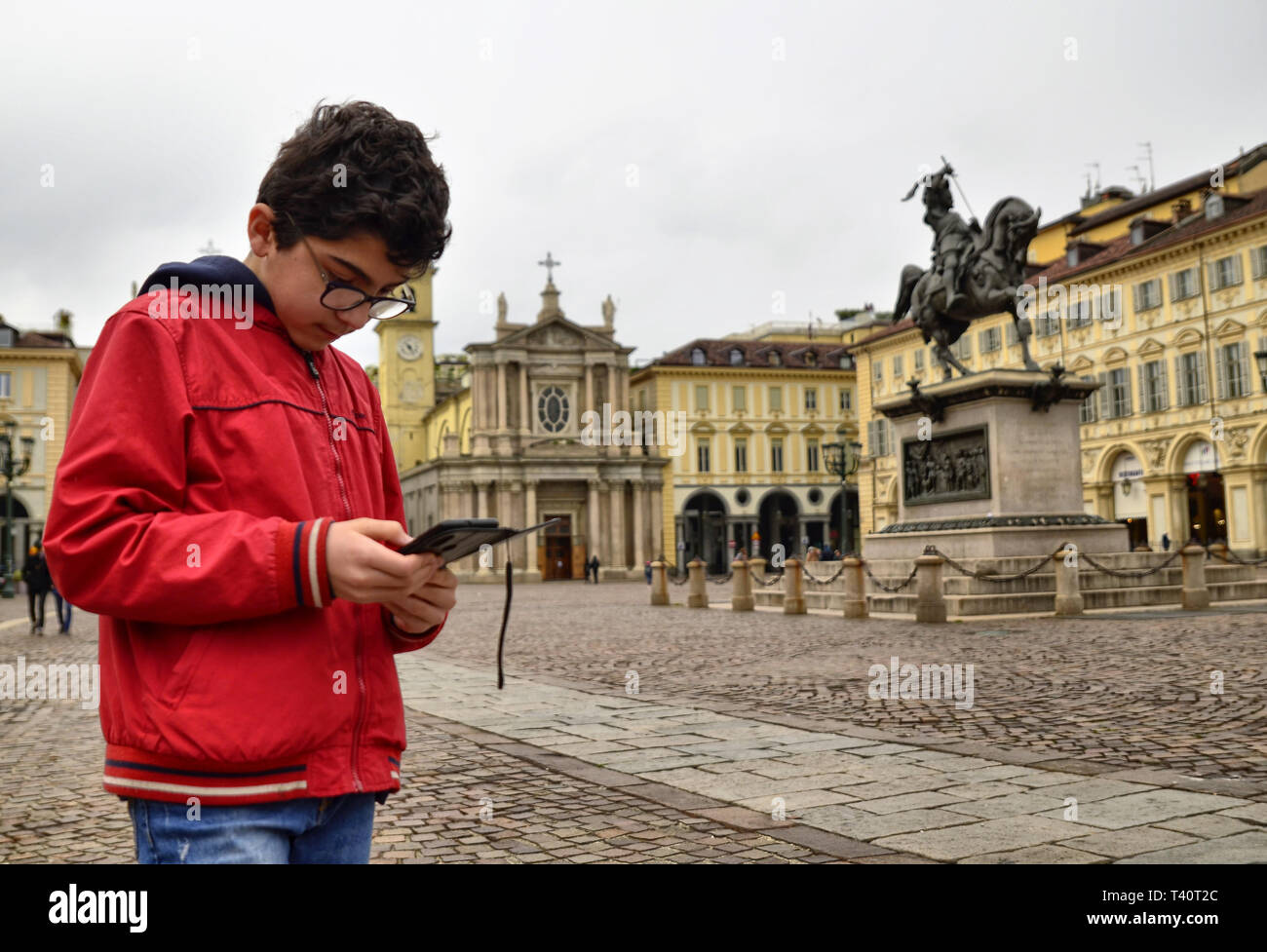 Turin, Piedmont, Italy. April 2019. In Piazza San Carlo people a child consults his smartphone. In the background the twin churches that characterize  Stock Photo