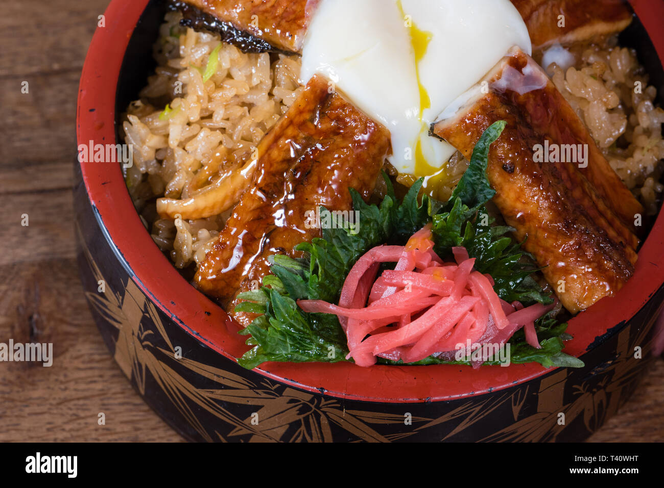 Japanese fusion dish with spicy rice with tamari sauce, roasted eel, egg and red turnip, in a decorated bowl, dark wood table background, details Stock Photo