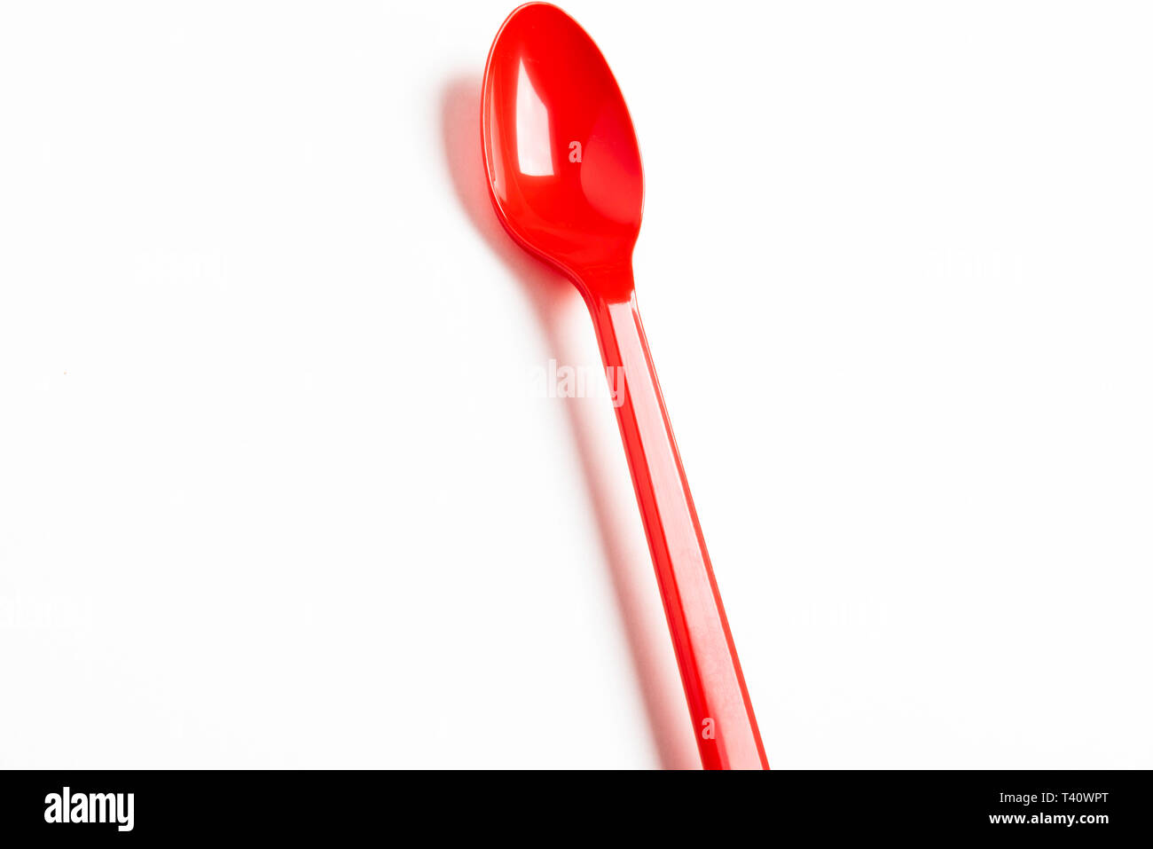 A red shiny long plastic spoon artistically set on a plain white