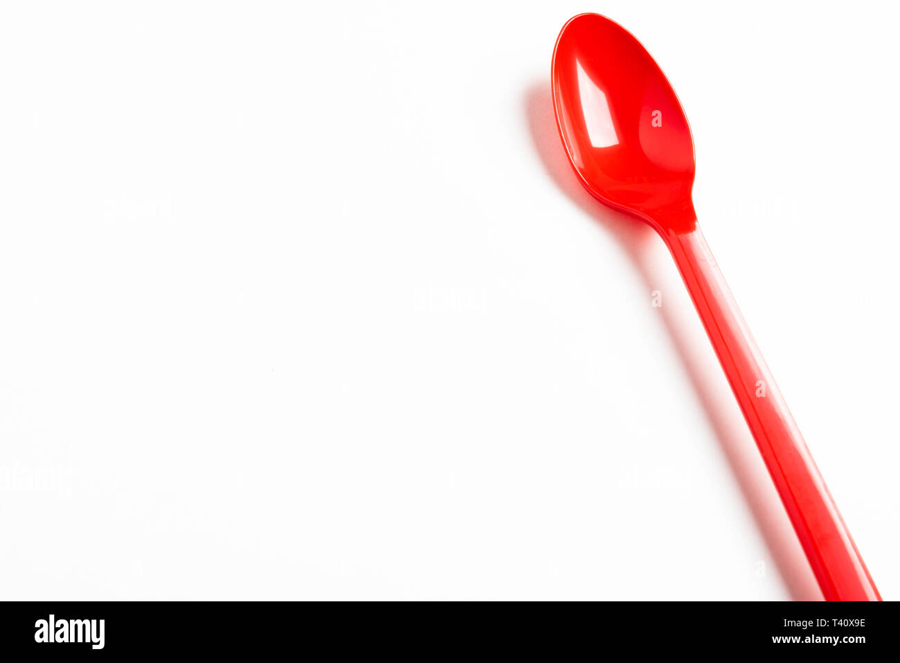 A red shiny long plastic spoon artistically set on a plain white