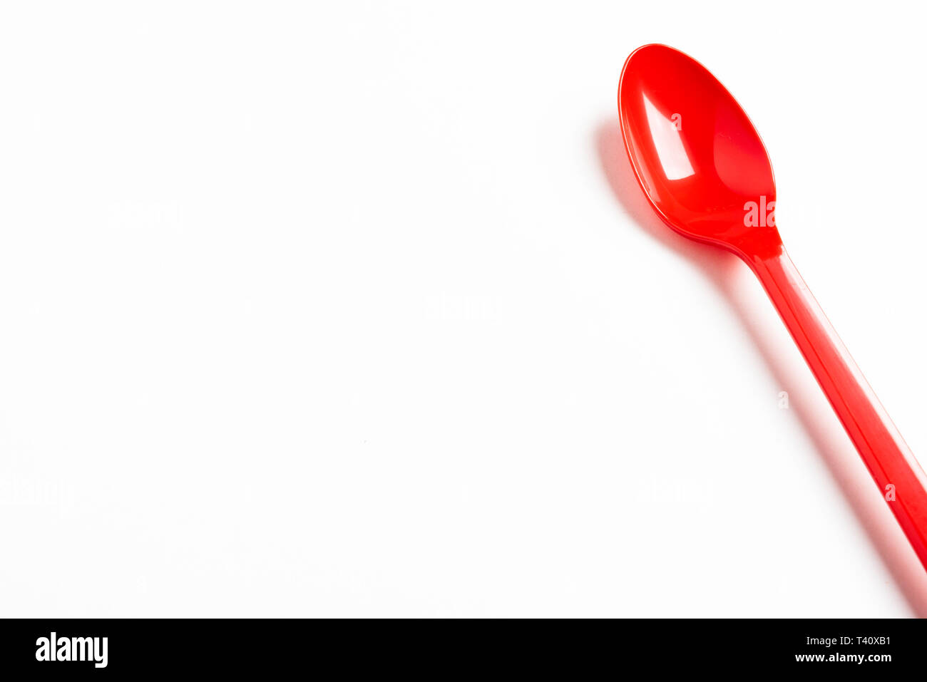A red shiny long plastic spoon artistically set on a plain white background with negative spaces. Stock Photo