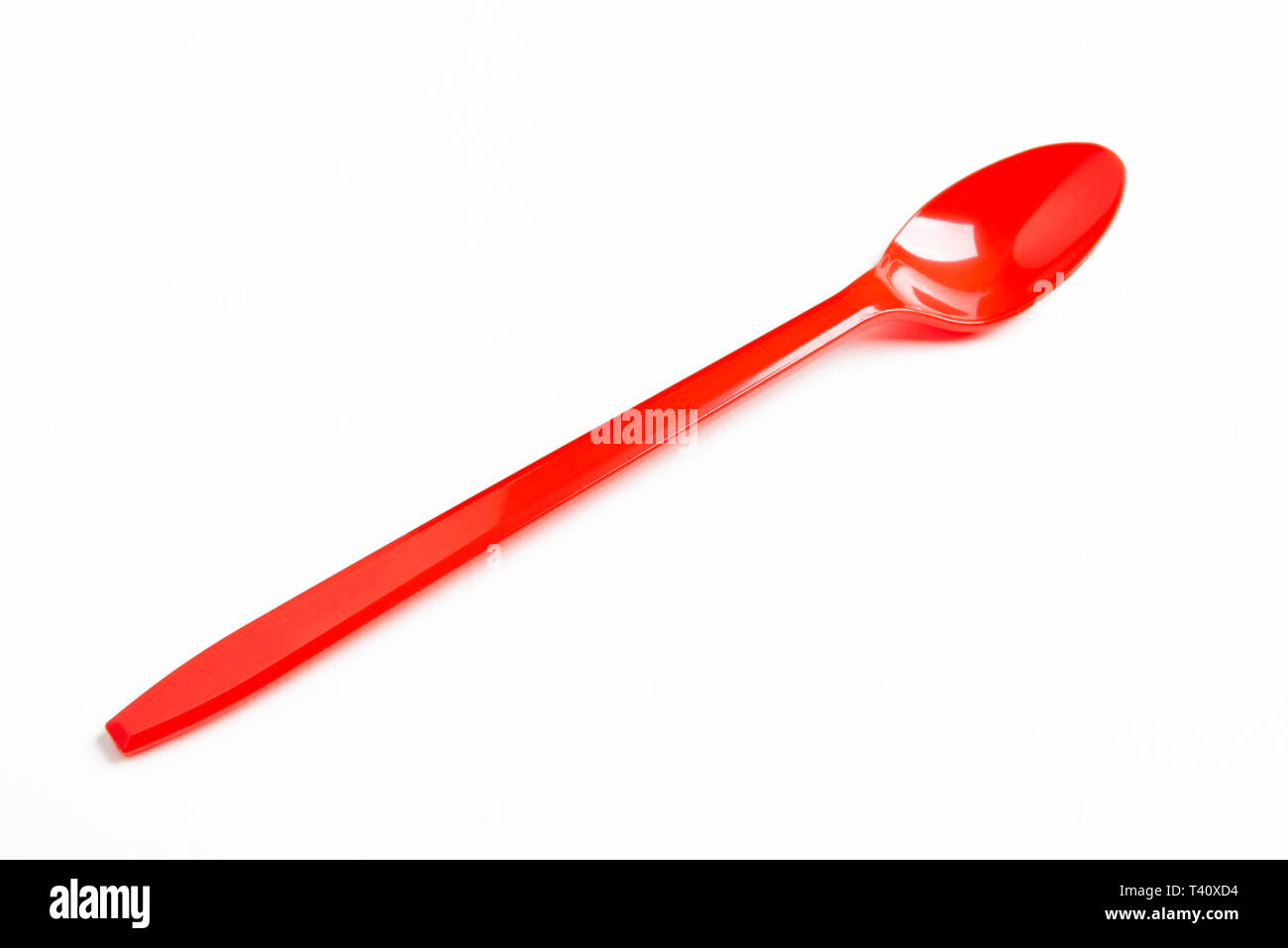 A red shiny long plastic spoon artistically set on a plain white background with negative spaces. Stock Photo