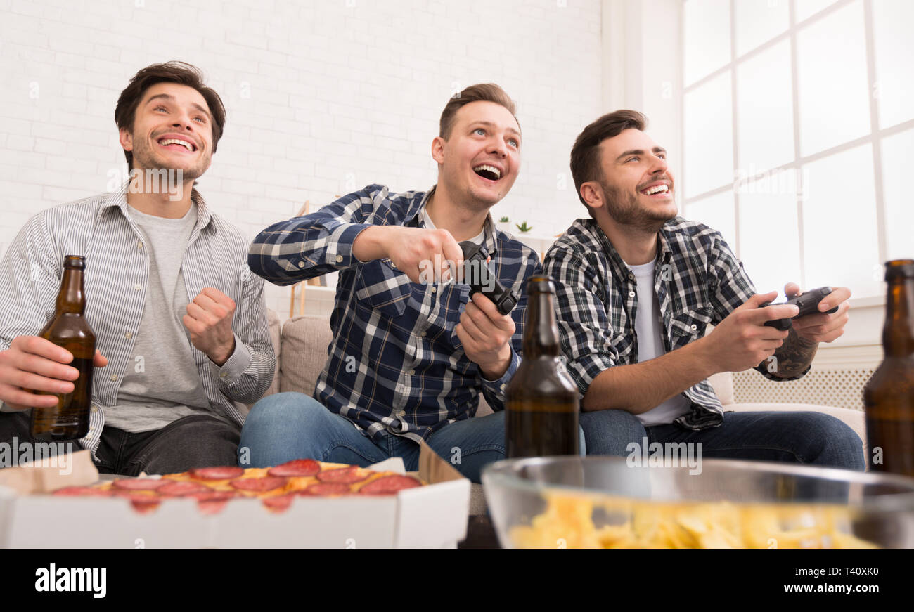 Excited men playing video game, having home party Stock Photo