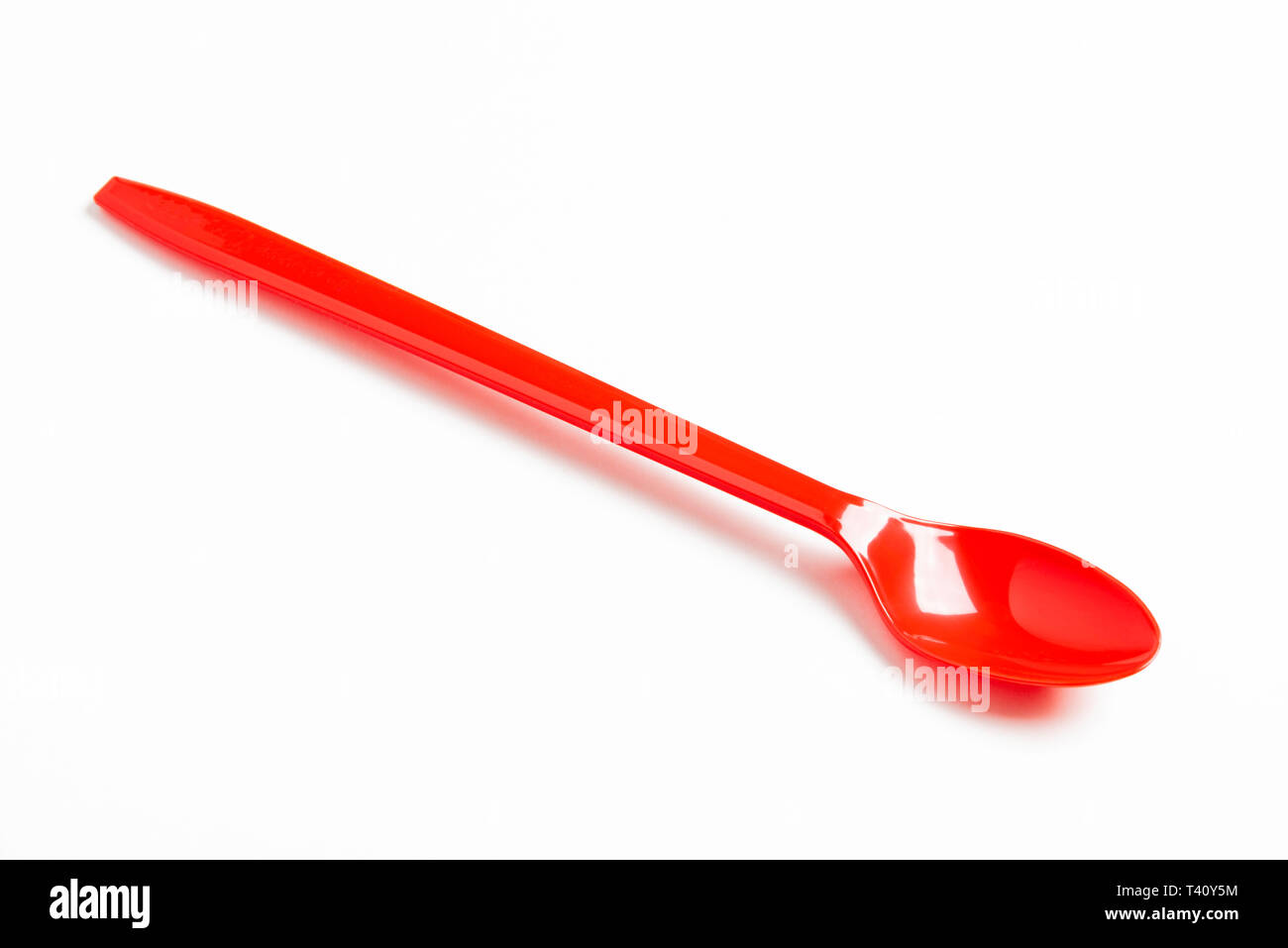 A red shiny long plastic spoon artistically set on a plain white