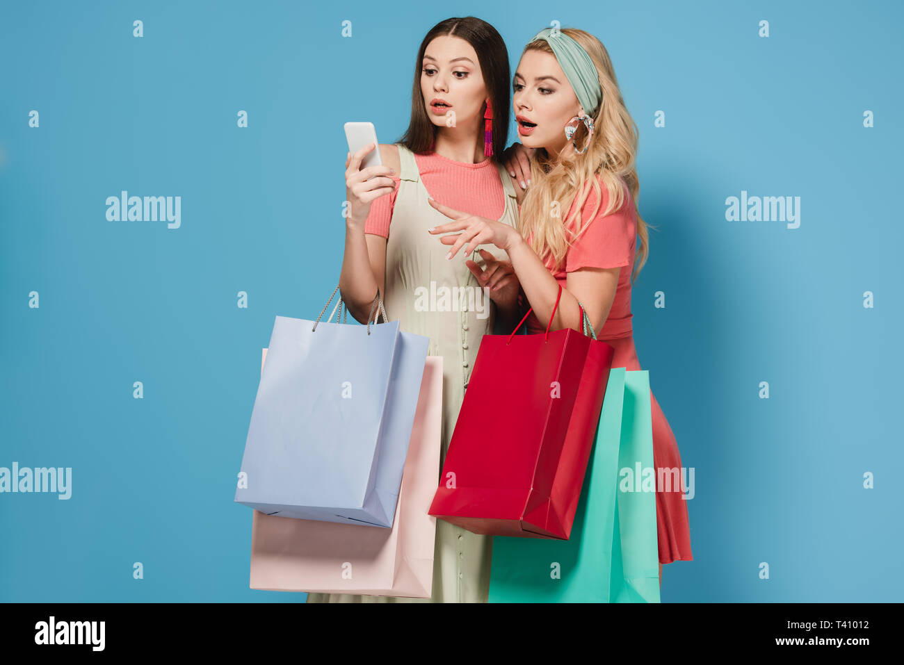 surprised brunette and blonde women in dresses holding shopping bags ...