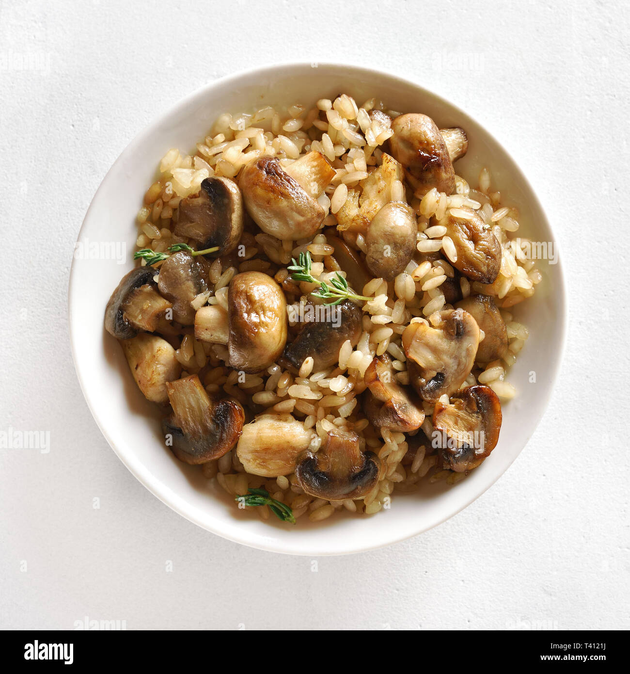 Close up of risotto with mushrooms and pieces of chicken meat in bowl over white stone background. Top view, flat lay Stock Photo