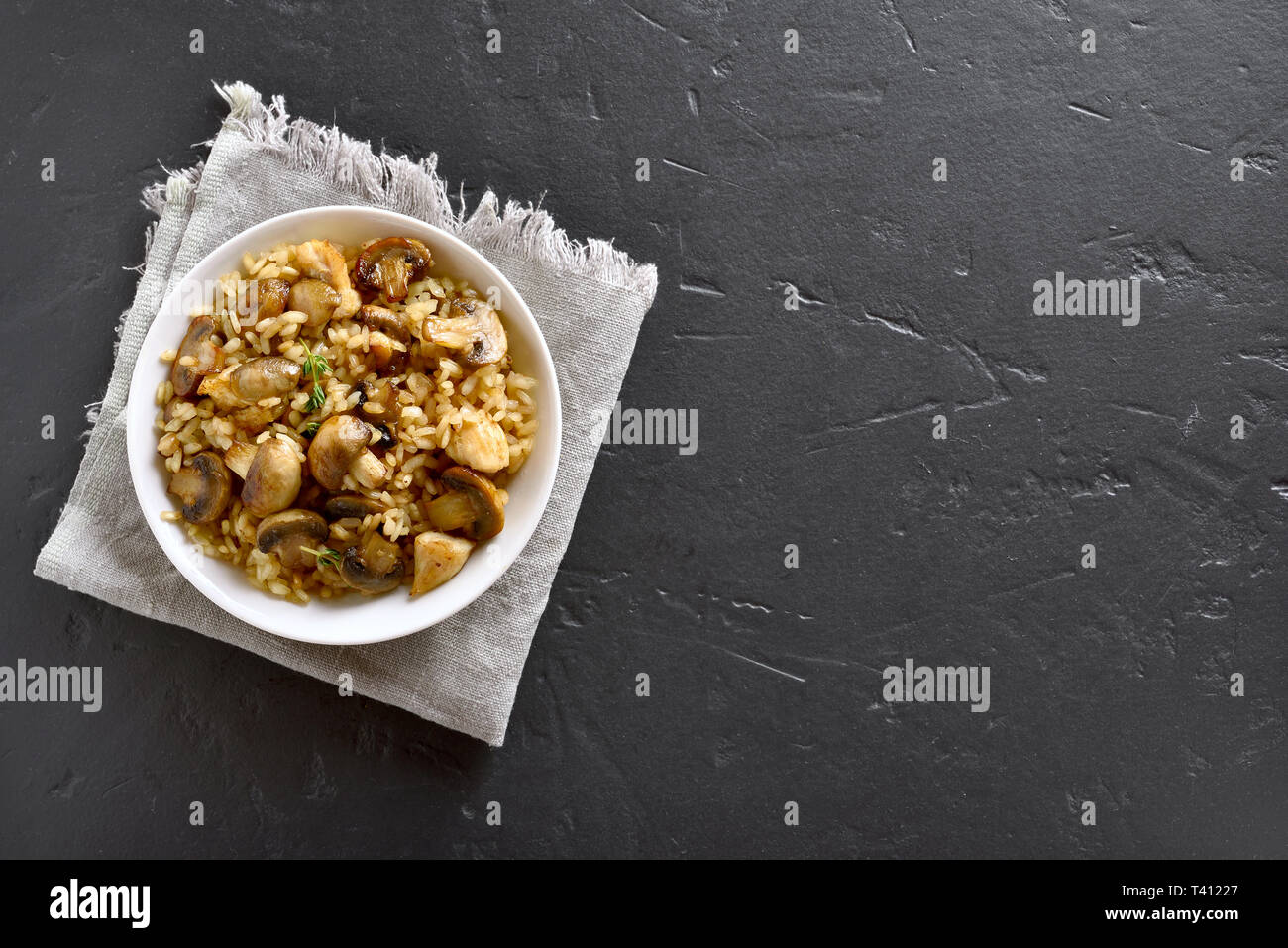 Risotto with mushrooms and pieces of chicken meat on black stone background with copy space. Top view, flat lay Stock Photo