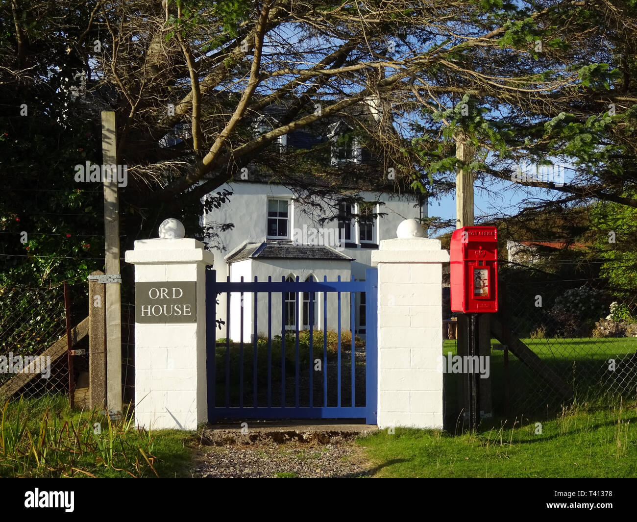 Scenic picture of Ord house on the Isle of Skye with a red royal mail letterbox, a blue gate, green trees and a white house combining four colours Stock Photo