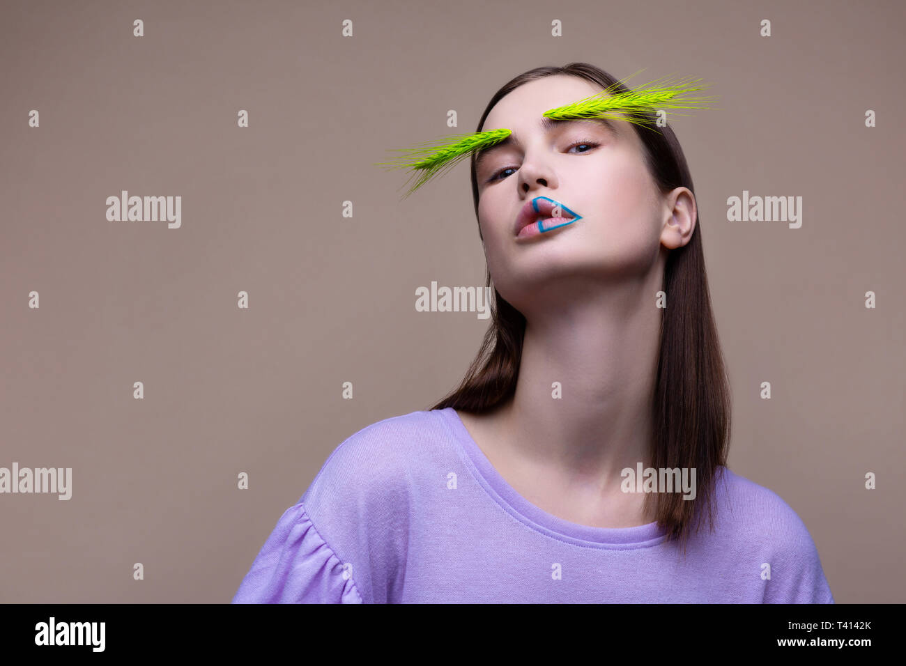 Model with blue lines on lips posing with green spikelet Stock Photo