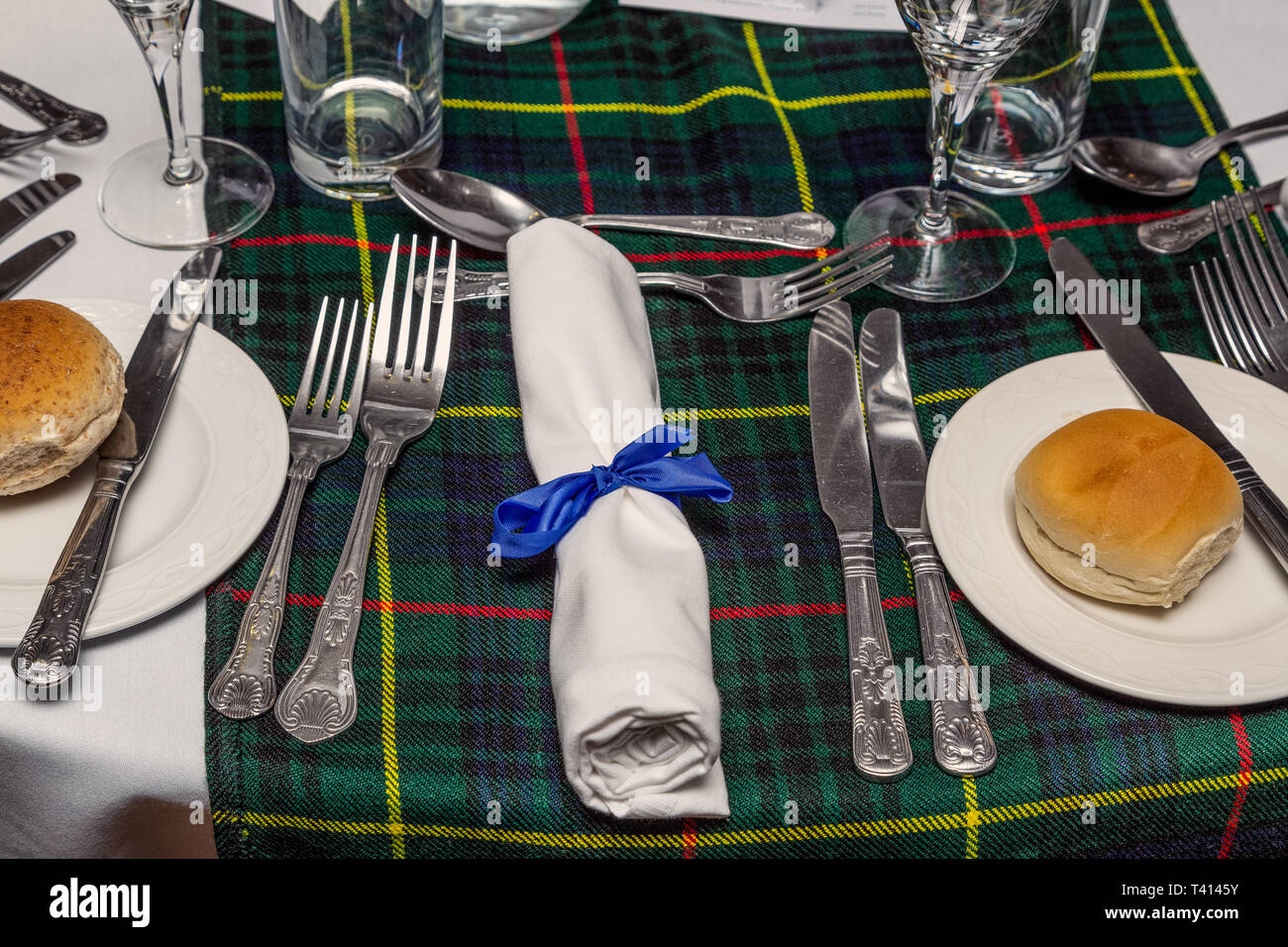 A Scottish dinner table with tartan table runner and a napkin in the centre with a blue bow around it. Stock Photo