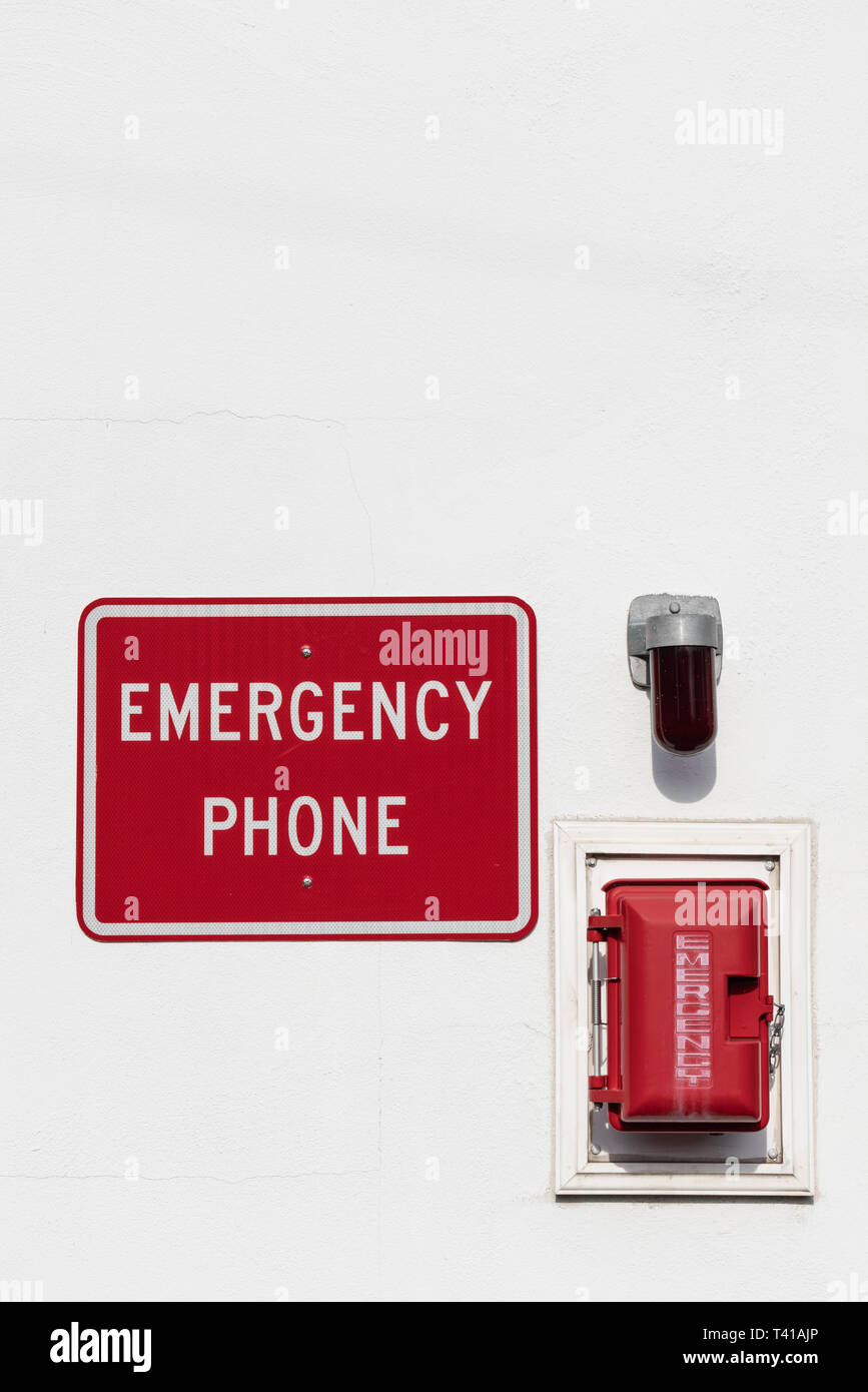 red emergency phone box on white wall with light and sign above outside