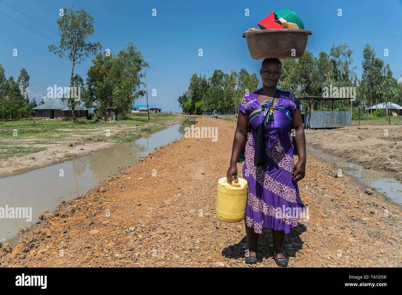 near Kisumu, Kenya - March 8, 2019 - a woman carries her belongings on the top of her head Stock Photo