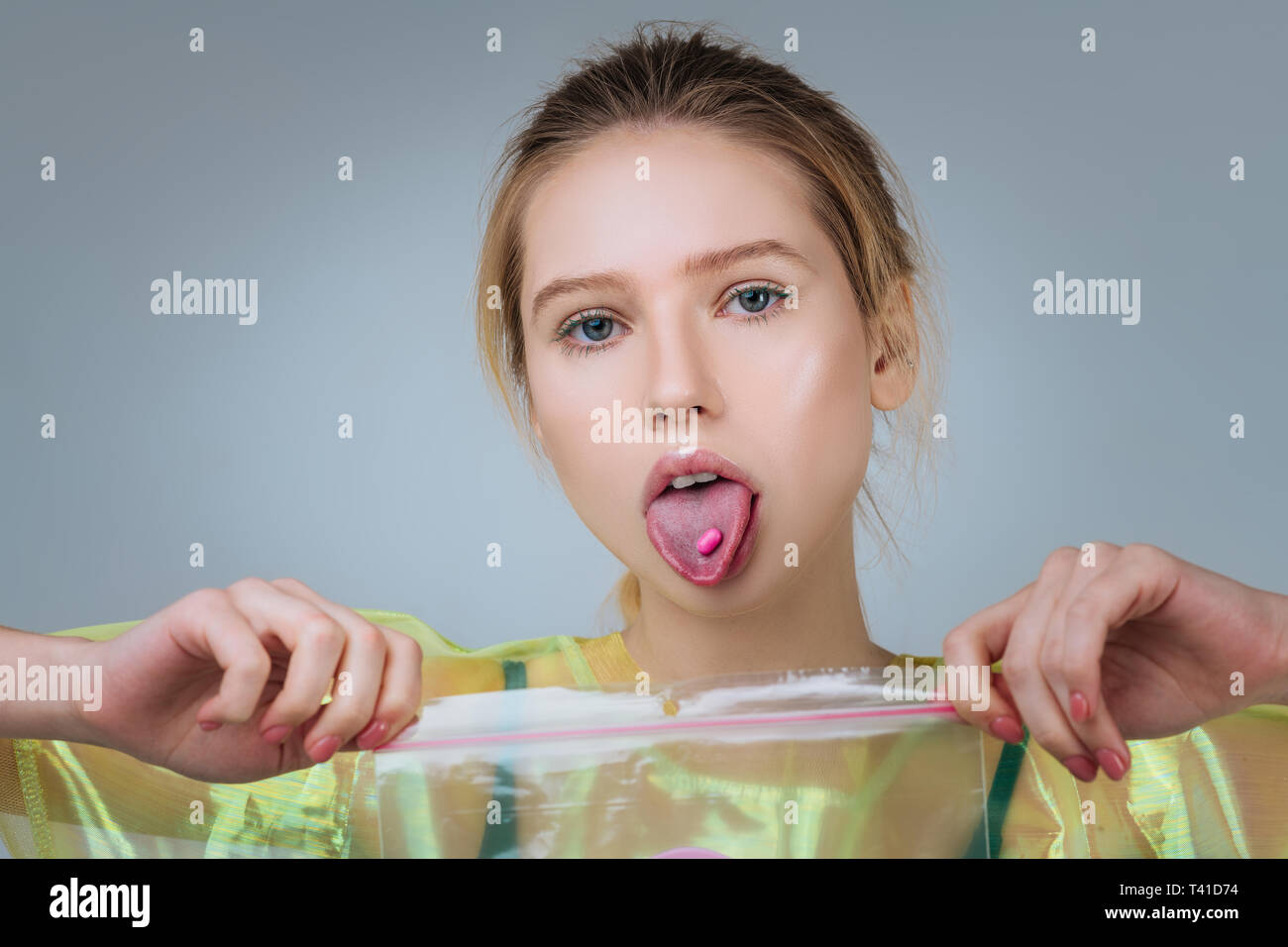Showing her tongue. Extravagant blue-eyed young model showing her tongue with pink pill on it Stock Photo